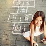 Beautiful Cheerful Little Girl Playing Hopscotch On Playground