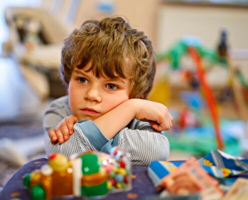 Portrait Of Little Kid Boy Sad On Birthday. Child With Lots Of Toy