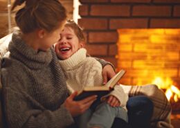 Happy Family Mother And Child Daughter Read Book On Winter Evening Near Fireplace